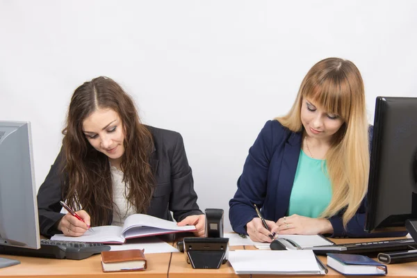 Dos mujeres de negocios que escriben en documentos en papel sentadas en un escritorio —  Fotos de Stock