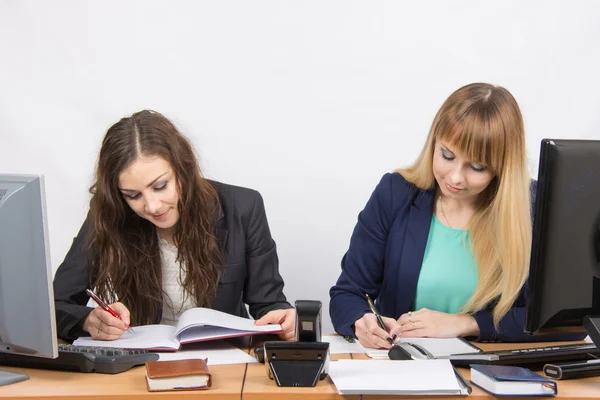 Due donne d'affari che scrivono in documenti cartacei sedute ad una scrivania — Foto Stock