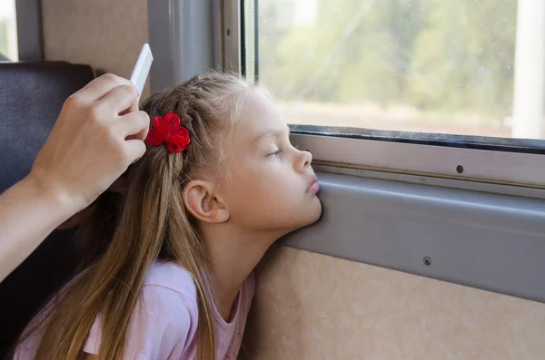 Uma menina triste olha para a janela enquanto está sentada em um trem elétrico até que minha mãe penteie seu cabelo comprido — Fotografia de Stock