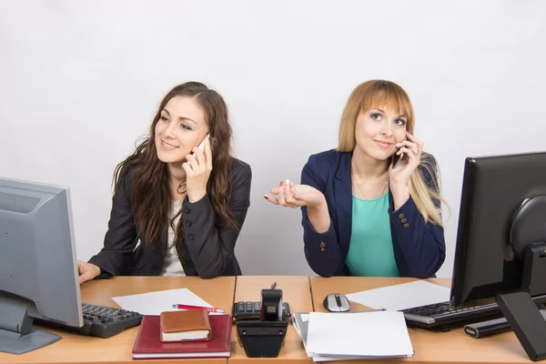 Две девушки за столом разговаривают по мобильному телефону в офисе — стоковое фото