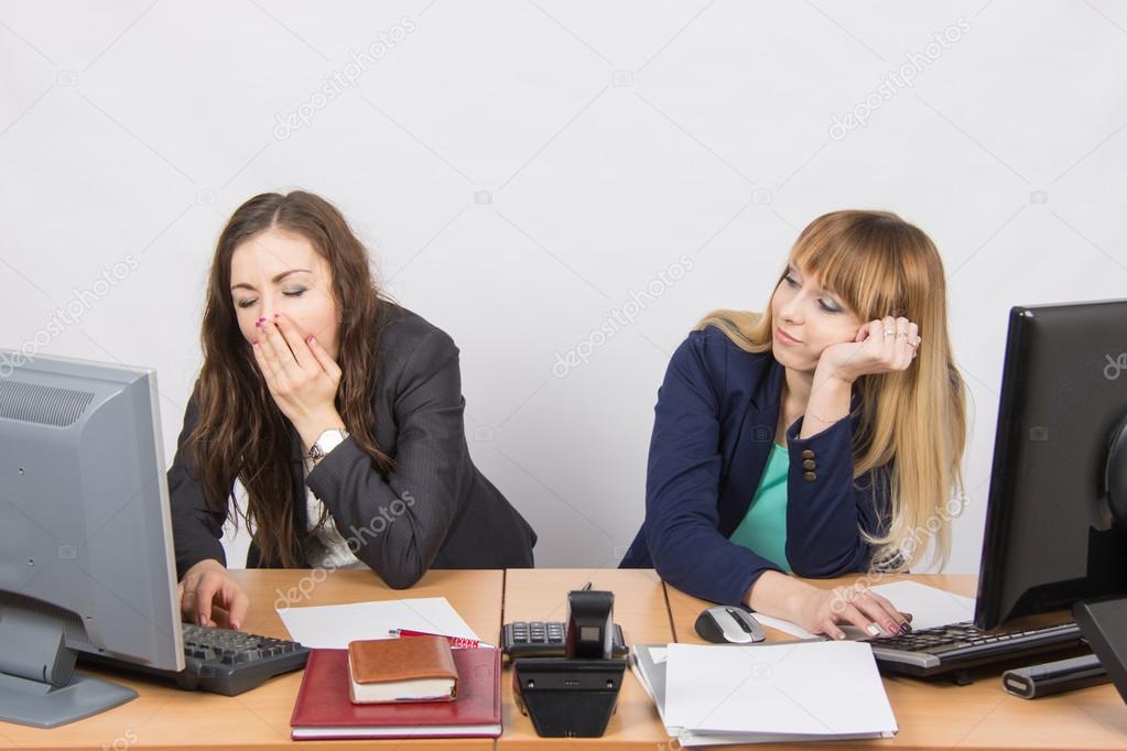 Two young office employee wearily sitting behind a desk