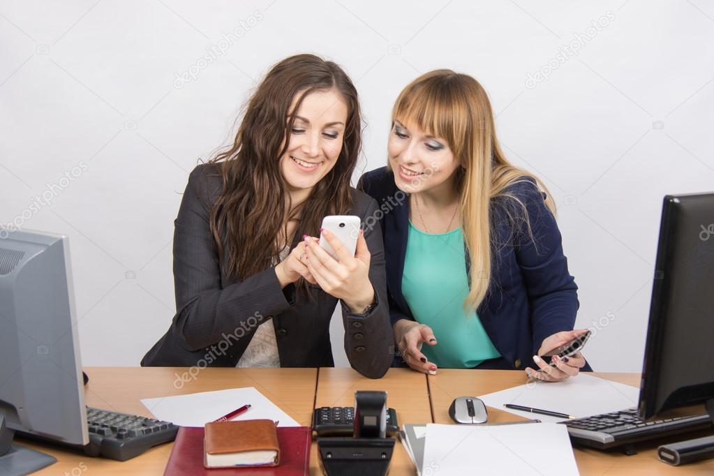 Two branchless workers enthusiastically looking at cell phone at his desk
