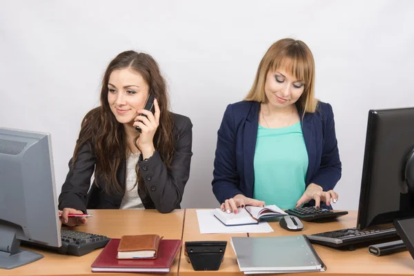 Office kollegor flicka sitter bakom ett skrivbord, med en telefon, den andra med en miniräknare — Stockfoto