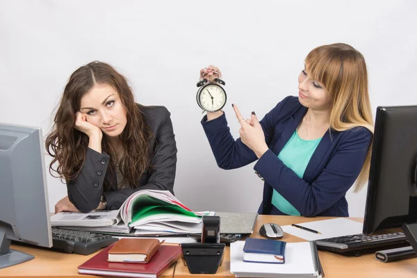 Gli impiegati alla fine della giornata, uno con un sorriso indica un orologio, un altro stanco puntelli testa — Foto Stock