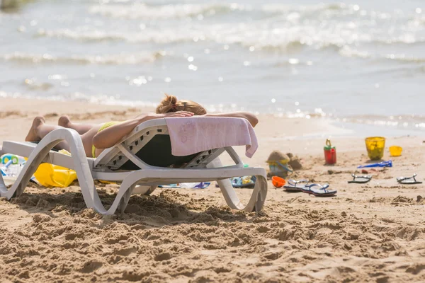 Στη θάλασσα παραλία κοντά στο νερό με μια καρέκλα παραλίας κορίτσι ηλιοθεραπεία, χαστούκια και τα παιδικά παιχνίδια άμμου — Φωτογραφία Αρχείου