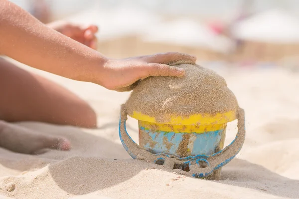 Los niños pluma en el cubo vierte arena en la playa —  Fotos de Stock