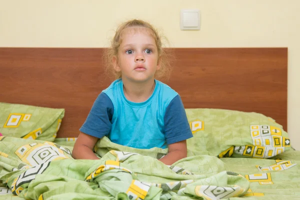Little girl sitting on a double bed and frightened looks into the distance — Stock Photo, Image