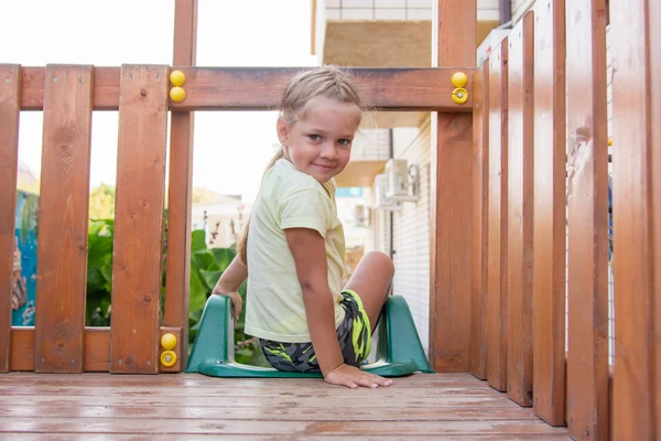 Четырехлетняя девочка сидит на деревянной площадке персонального игрового комплекса — стоковое фото