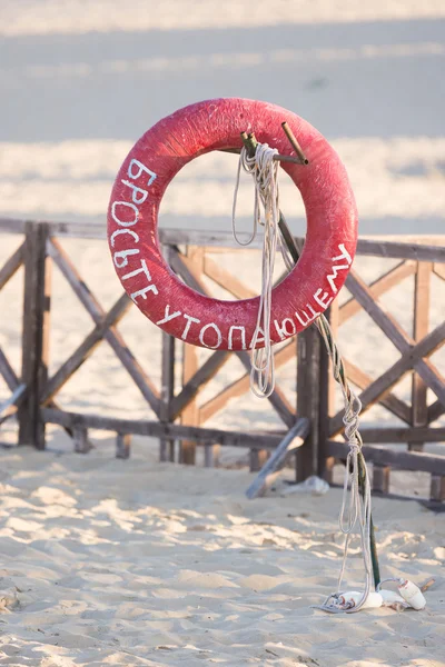 Rettungsring wirft einen Ertrinkenden mit einem Schild, das an einem rostigen Metallstab hängt, an den Sandstrand — Stockfoto