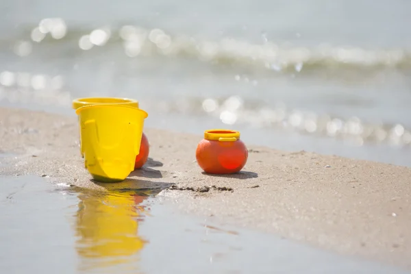 Παιδικά πιάτα παιχνίδι αντικείμενα αριστερά στην αμμώδη ακτή δίπλα στο νερό — Φωτογραφία Αρχείου