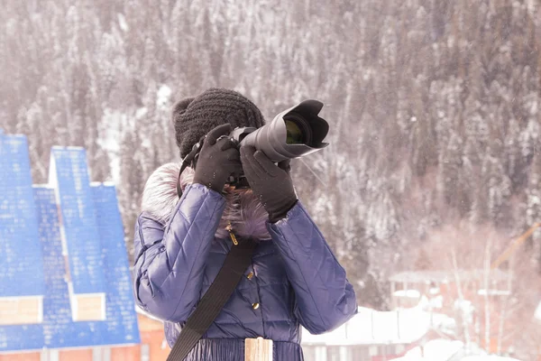 En ung flicka tar bilder vintern bergslandskap i snöstorm på en Slr-kamera med teleobjektiv — Stockfoto