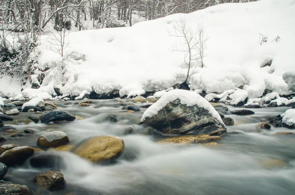 Rio de montanha que flui rapidamente em um fundo de floresta coberta de neve, turva por uma velocidade lenta do obturador — Fotografia de Stock