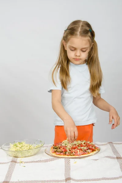 Küçük altı yaşındaki kız masada duran ve rendelenmiş peynir pizza serpin — Stok fotoğraf