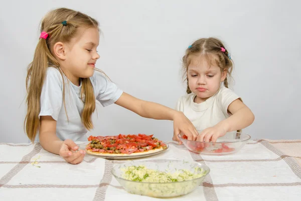 テーブルの上の2人の小さな女の子がトマトピザに広がる — ストック写真