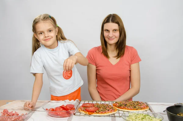 Шестилетняя девочка надевает помидоры для пиццы под присмотром мамы — стоковое фото