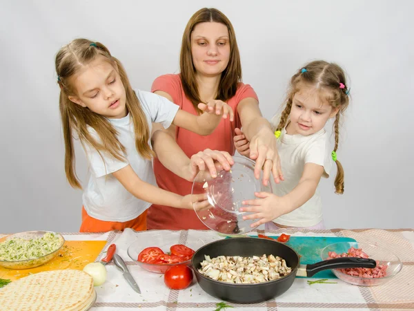 Mãe com duas filhas na mesa da cozinha com um prato de cogumelos é derramado na panela — Fotografia de Stock