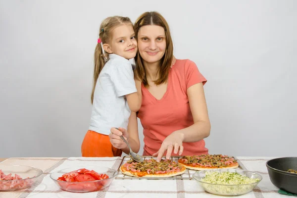 Dotter kramar sin mamma, vilket gör pizza vid bordet — Stockfoto