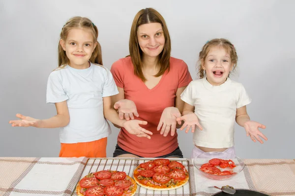 Mom with two young daughters happily show made pizza with tomatoes — Stock Photo, Image