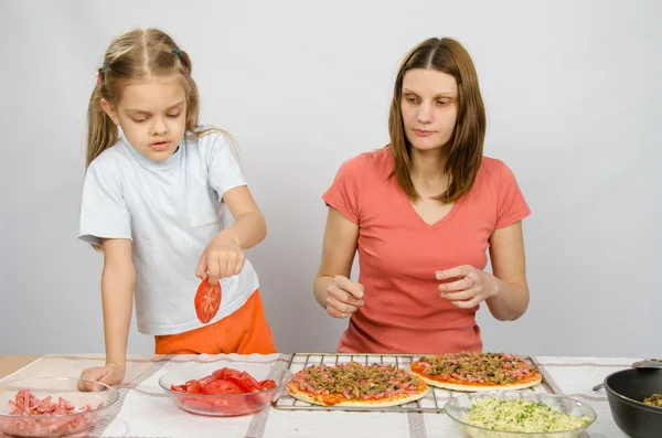 Six year old girl takes a plate of cutting tomatoes for pizza under the supervision of mum — Stock Photo, Image