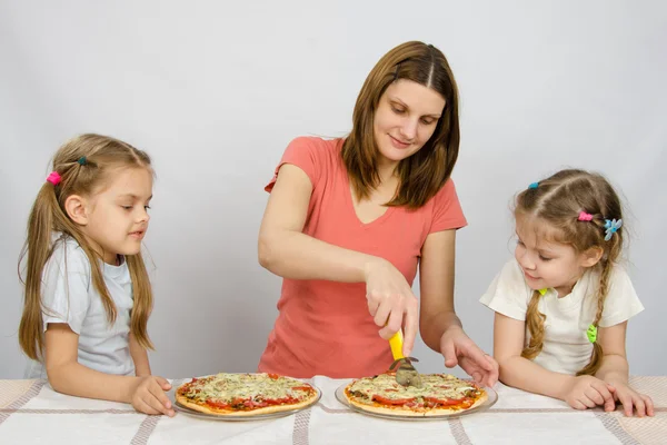 Мама режет пиццу, и две маленькие девочки с нетерпением смотрят — стоковое фото