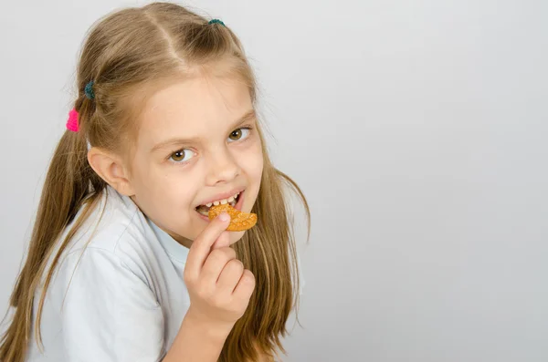 Porträtt av en liten sexårig flicka som biter en cookie — Stockfoto