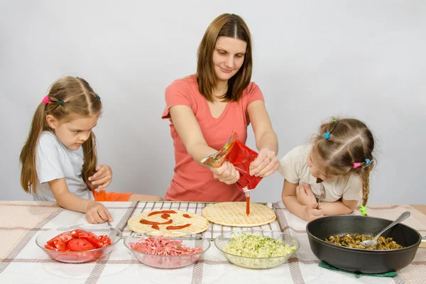 Dwie dziewczynki entuzjastycznie patrzył jak mama wylewa ketchup podstawa pizzy — Zdjęcie stockowe