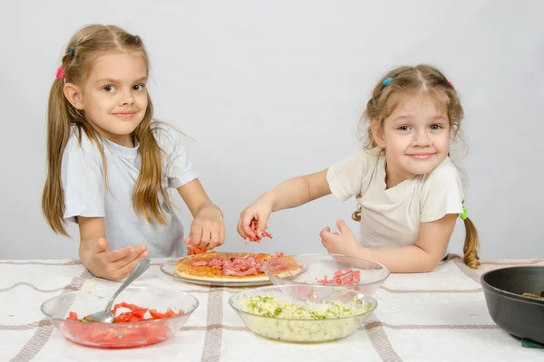 Two little happy girl at the table spread on the pizza ingredients — Stock Photo, Image