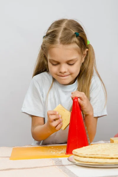 Six-year girl posing at the kitchen table with cheese and a grater in the hands of — Stock Photo, Image