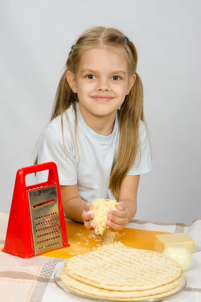 The little girl at the table rubbed grated cheese for pizza — Stock Photo, Image