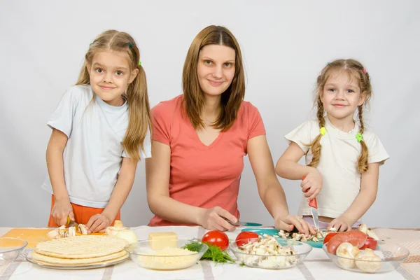 Woman with two young girls at the table prepared ingredients for pizza — Stock Photo, Image