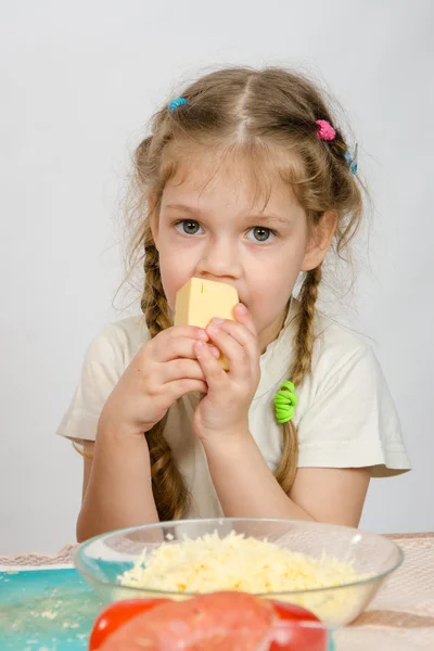 Five-year girl with pigtails eating cheese at the table in front of her is a plate of grated cheese — Stock Photo, Image