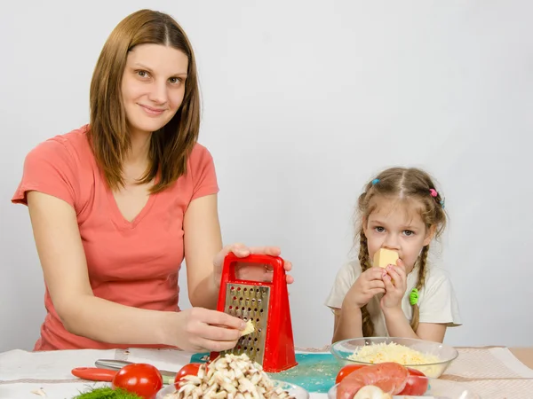 La fille à la table de la cuisine t râpe à fromage assis à côté d'une fille de cinq ans et mange du fromage — Photo