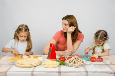 Memnun anne mutfak masasında kesme ürünlerini yardımcı olmak için küçük kızı izlerken