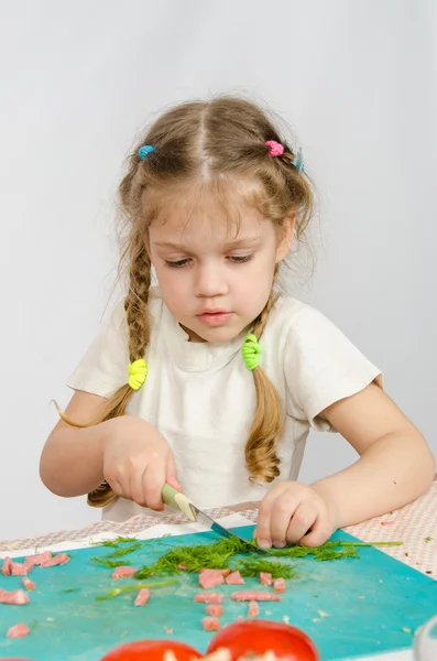 Little six year old girl intently trying to cut with a knife green kitchen table — Stock Photo, Image