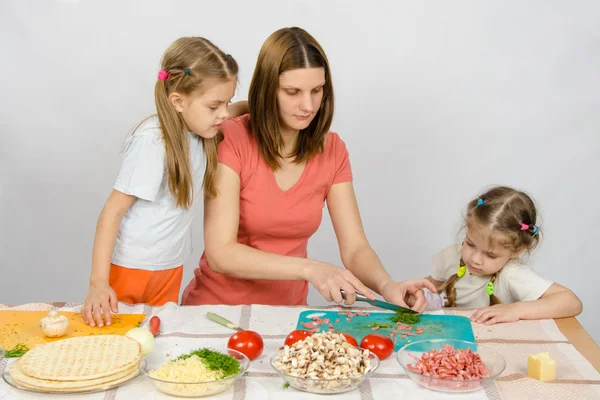 Two daughters are watching with interest as the mother chopped green — Stock Photo, Image