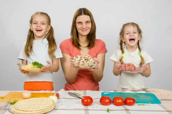 Mother with two daughters happily holding a plate with sliced products for pizza — Stock Photo, Image