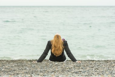 O bulutlu bir gün deniz kenarında bir çakıl sahilde oturur, kafası geri atılır