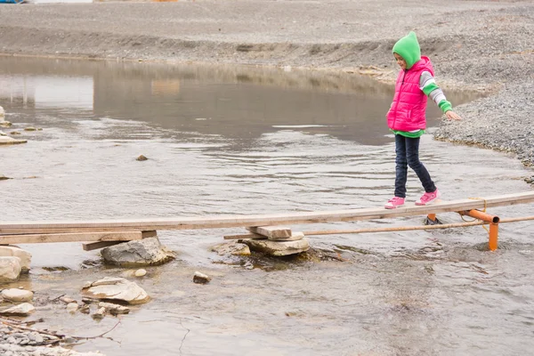 Маленькая девочка осторожно идет на доску через пруд — стоковое фото