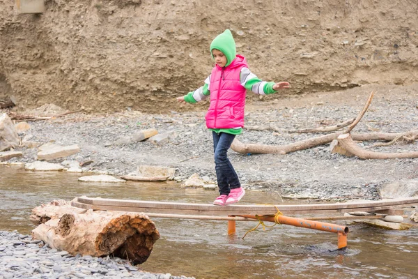 Ragazza sette anni è sul ponte traballante sopra le braccia torrente disteso per l'equilibrio — Foto Stock