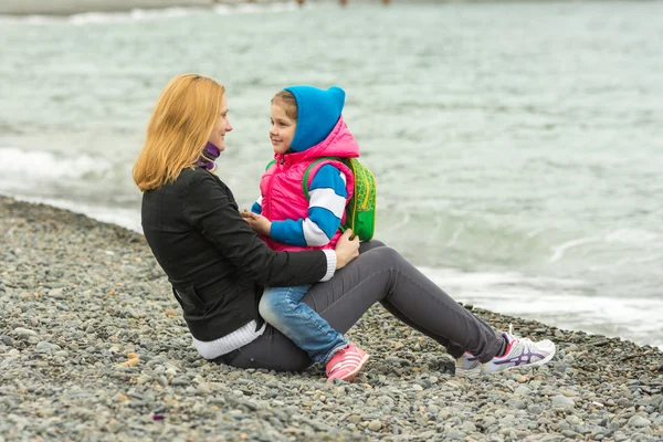 Mutter und Tochter schauen einander an einem kühlen Tag zärtlich am Strand sitzend an — Stockfoto