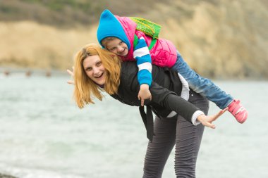 Genç kız sahilde küçük bir kız arkası soğuk havada binmek eğleniyor