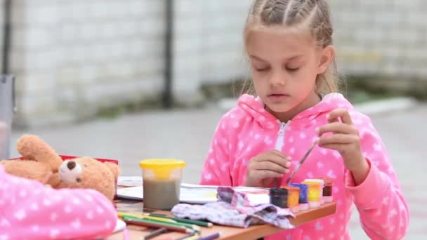 Chica de siete años elegir el dibujo de tinta de color adecuado en un álbum, sentado en una mesa con otra chica — Vídeo de stock