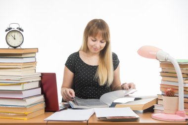 Bir öğrenci bir gülümseme ile kütüphanede kitap ile çevrili bir masada bir klasördeki sayfaları çevirme