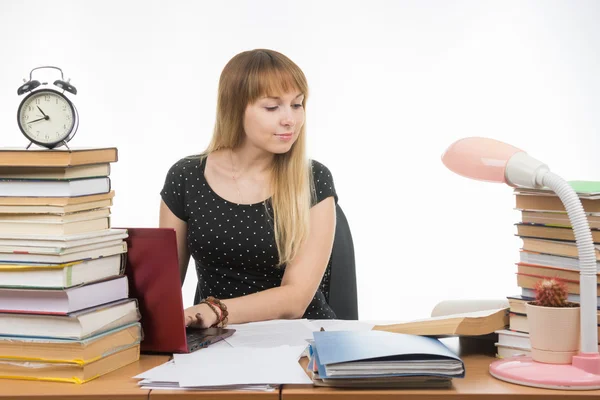 Studente universitario sorridente con un computer portatile per ottenere informazioni mentre seduto a un tavolo disseminato di libri in biblioteca — Foto Stock