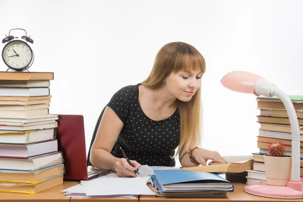 Bella studentessa a un tavolo disseminato di libri in biblioteca lavoro di scrittura — Foto Stock