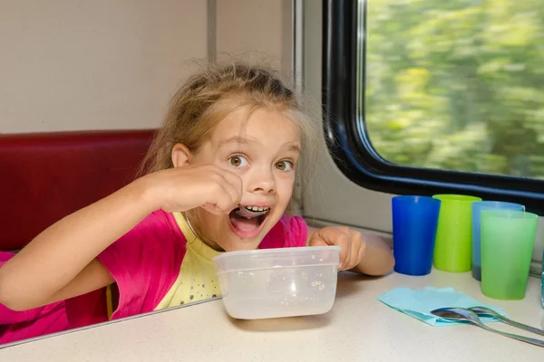 A menina no trem senta-se em uma mesa no lugar mais baixo no compartimento de segunda classe do carro e come-o com colher saborosa — Fotografia de Stock