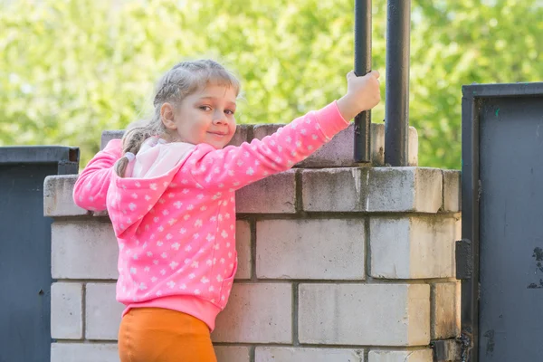 Pięć lat dziewczyna wspi się na ogrodzeniu cegły i odwrócił spojrzał na ramie — Zdjęcie stockowe