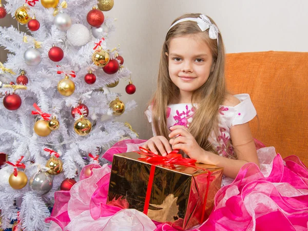 Siete años chica en un hermoso vestido se sienta con un regalo en sus manos —  Fotos de Stock