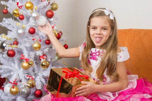 Zevenjarig meisje in een mooie jurk zit met een geschenk en toonde taal naar frame — Stockfoto