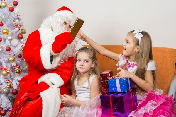 Санта Клаус дарит подарки одной девушке, а другой сидит в ожидании — стоковое фото